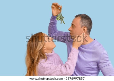 Mature couple kissing under mistletoe branch on blue background