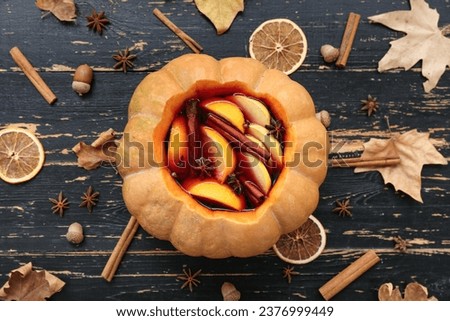 Beautiful composition with tasty mulled wine in pumpkin on black wooden background