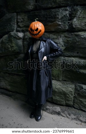 An adult model in a pumpkin head mask poses for a full-body portrait in front of a brick background under Glen Span Arch in Central Park