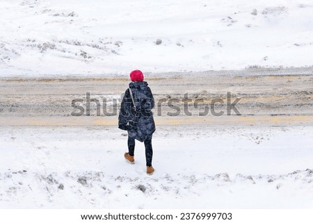 Woman crossing road during blizzard, low visibility in winter season. Woman walking in snowy day view form above. Female crossing road, extreme winter weather. Alone woman walk during snow storm Royalty-Free Stock Photo #2376999703