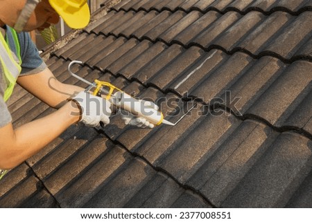 Worker man using silicone sealant adhesive  to fix crack of the old tile roof. Royalty-Free Stock Photo #2377008551