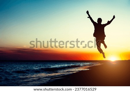 Silhouette young woman jumping with hands up on the beach at the sunset. Travel photo summertime