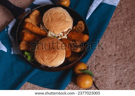 Overhead view of homemade chicken burger, cheese sticks and fried wiener sausages on a pan, comfort food breakfast on a calm autumn morning Royalty-Free Stock Photo #2377025005