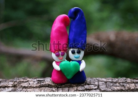 Two toy dwarfs made of plasticine hold a heart. Valentine's Day. A symbol of love.