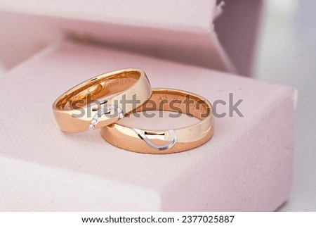 Pair of personalized gold wedding bands with diamond-studded detail, elegantly placed on a soft pink cushioned box. Royalty-Free Stock Photo #2377025887