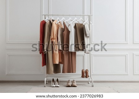 Rack with different stylish women`s clothes and shoes near white wall indoors Royalty-Free Stock Photo #2377026983