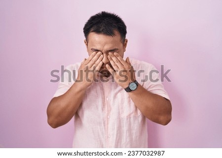 Chinese young man standing over pink background rubbing eyes for fatigue and headache, sleepy and tired expression. vision problem 