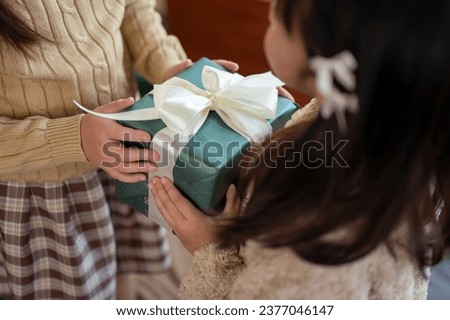 Close-up image of a young girl giving a Christmas gift to her friend or sister. Merry Christmas, present, birthday gift, special moment