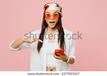Young latin woman she wears white shirt casual clothes sunglasses hold in hand use point finger on mobile cell phone browsing internet isolated on plain pastel light pink background. Lifestyle concept