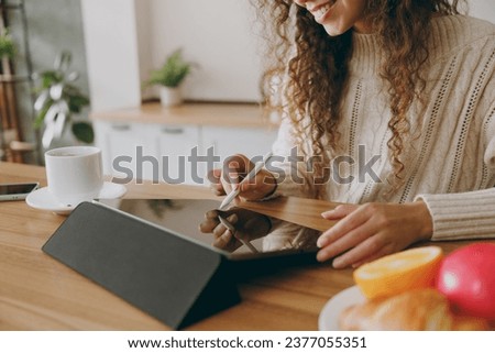 Cropped young graphic designer housewife woman wears casual clothes sweater hold in hand work use write draw stylus pc pen sit at table in light kitchen at home alone. Lifestyle cooking food concept Royalty-Free Stock Photo #2377055351