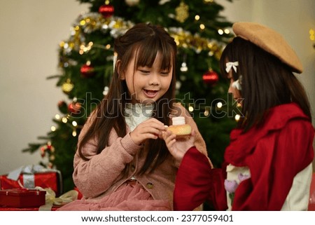 Happy little children eating cake with a beautifully decorated Christmas tree on background.