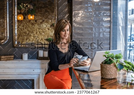 Sophisticated woman using her smartphone and laptop in a street- Royalty-Free Stock Photo #2377061267