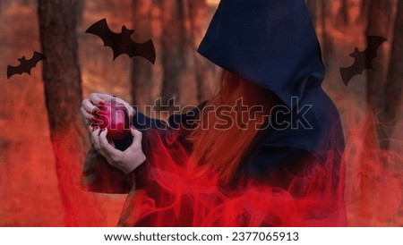 Halloween, red-haired Witch with an apple in a dark forest. A girl in the smoke performs witchcraft.