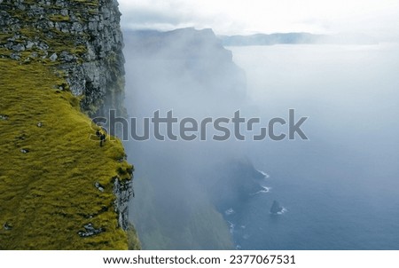 Hiker standing on edge of famous rock cliff. Concept: Adventure, Explore, Hike, Lifestyle. Faroe Islands. Dramatic weather Royalty-Free Stock Photo #2377067531