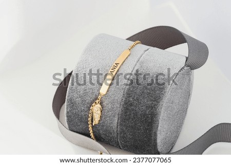 A personalized gold necklace with the name inscribed on a bar pendant, elegantly draped over a textured gray jewelry box, accented by a dark ribbon, emanating sophistication and style. Royalty-Free Stock Photo #2377077065