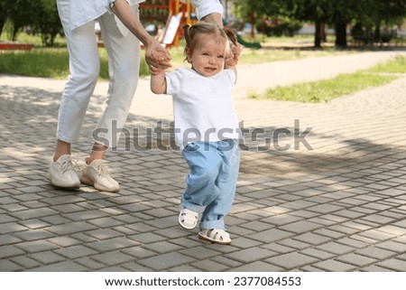 Mother supporting daughter while she learning to walk outdoors, closeup. Space for text