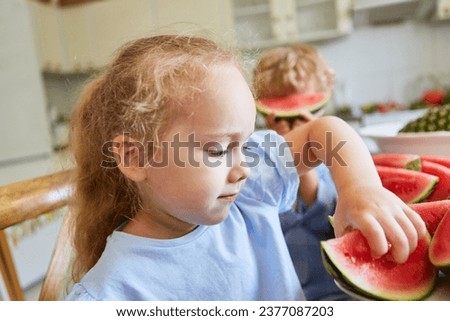Cute blond girl holding fresh watermelon slice in kitchen at home
