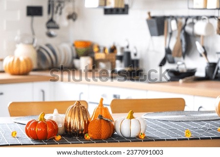 Decor of white classic kitchen with pumpkins, garlands, latern for Halloween and harvest with figurine of house. Autumn mood in home interior, modern loft style. real estate, insurance, mortgage
