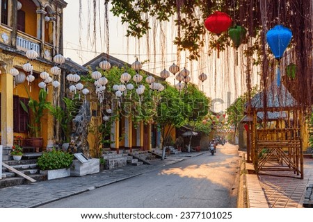 Gorgeous view of cozy street decorated with colorful silk lanterns at sunrise. Scenic traditional old yellow houses of Hoi An Ancient Town, Vietnam. Hoian is a popular tourist destination of Asia. Royalty-Free Stock Photo #2377101025