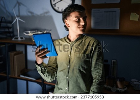 Non binary person using touchpad device at night looking to side, relax profile pose with natural face and confident smile. 