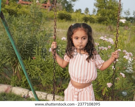 Little girl playing on swinging and jumping.Wearing pink lining dress with blur background.Smiling on face looks beautiful.Having fun in park.Portrait image editing filter effect.