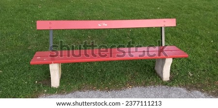 Red parkbench with gras around, standing in a park on a sunny day. Royalty-Free Stock Photo #2377111213