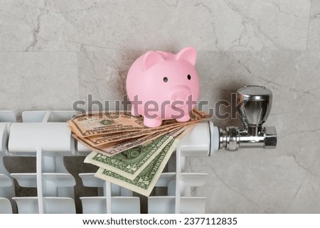 Savings concept.Money in piggy bank on radiator on a gray wall background. Concept of heating season. Concept of expensive heating costs and rising energy bill prices for winter cold season.