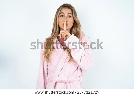 Surprised Young beautiful woman makes silence gesture, keeps finger over lips and looks mysterious at camera
