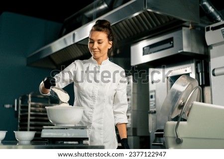 A female baker in a white chef's tunic kneads dough to prepare and bake bread in the bakery Royalty-Free Stock Photo #2377122947
