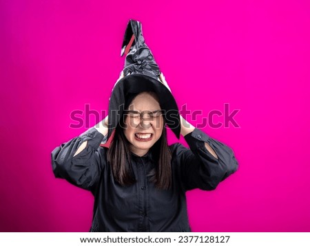 Portrait of an Asian Indonesian woman wearing a Halloween-themed costume with a witch hat, screaming in distress while holding her head. Isolated against a magenta background.