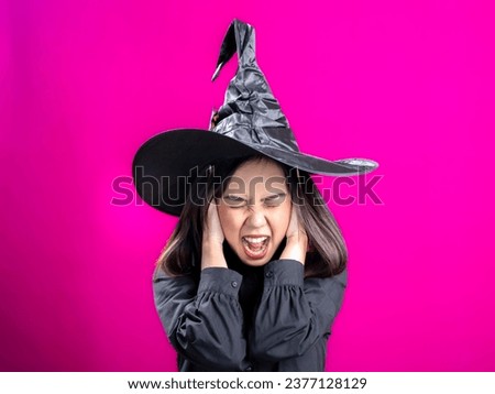 Portrait of an Asian Indonesian woman wearing a Halloween-themed costume with a witch hat, screaming in distress while holding her head. Isolated against a magenta background.