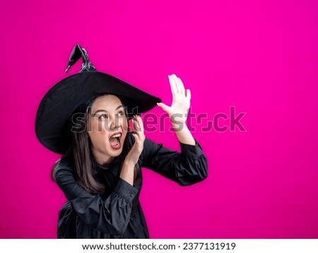 Portrait of an Asian Indonesian woman wearing a Halloween-themed costume with a witch hat, looking scared with a frightened pose. Isolated against a magenta background.
