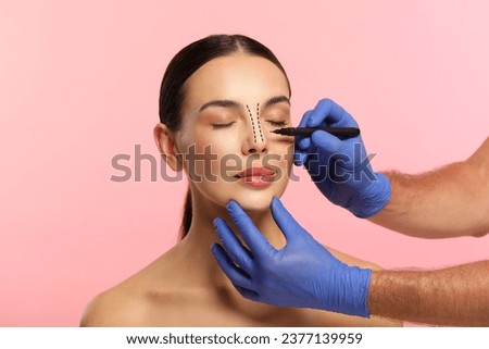 Woman preparing for cosmetic surgery, pink background. Doctor drawing markings on her face, closeup Royalty-Free Stock Photo #2377139959