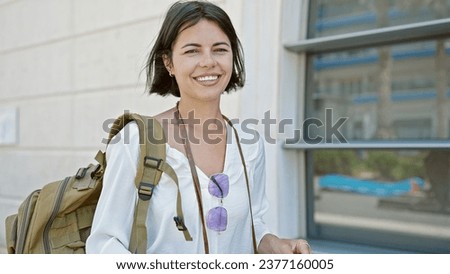 Young beautiful hispanic woman tourist smiling confident wearing backpack at street