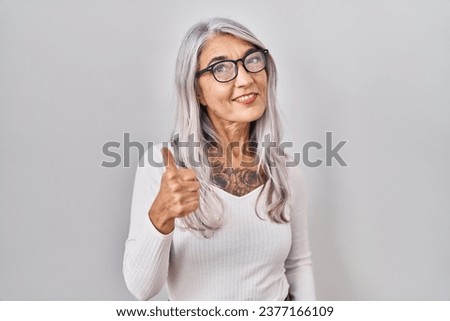 Middle age woman with grey hair standing over white background doing happy thumbs up gesture with hand. approving expression looking at the camera showing success. 