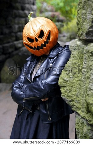 An adult model wearing a pumpkin head mask poses for a portrait by leaning against the stones of the Glen Span Arch with crossed arms