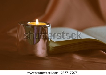 Madrid, Spain May 1, 2023 Open hardcover paper book, turning pages. Reading literature by candlelight. Burning candle in a stylish candle holder. A cozy evening at home. Knowledges, studying, read. Royalty-Free Stock Photo #2377179071