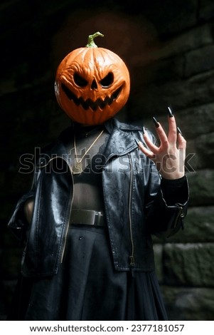 An adult model wearing a pumpkin head mask makes claw-like gestures to the camera with long, black, press-on nails                          