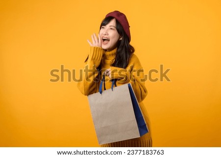 Young Asian woman 30s, wearing a yellow sweater and red beret, shouting to free space with shopping paper bag against a vibrant yellow backdrop.