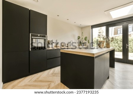 a modern kitchen with black cabinetry and wood flooring in an open plan living room, dining area on the other side Royalty-Free Stock Photo #2377193235