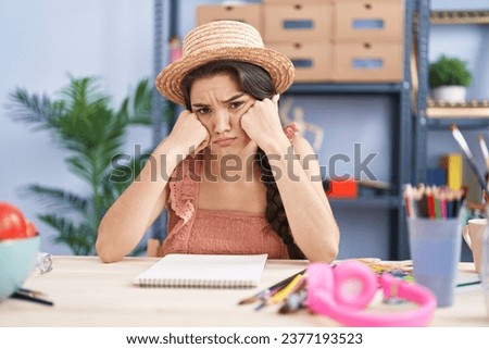 Young hispanic woman artist sitting with sad expression at art studio