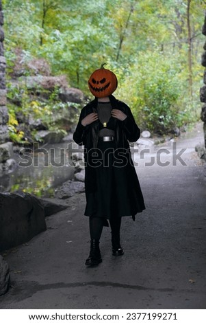 An adult model wearing a pumpkin head mask holds their leather jacket while posing for a full body portrait under the Glen Span Arch