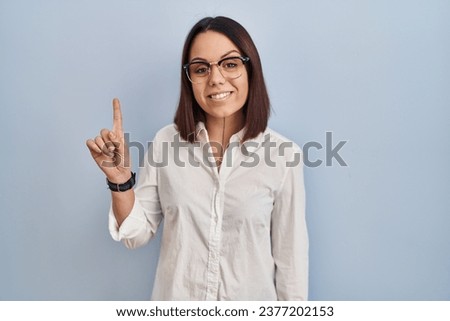 Young hispanic woman standing over white background showing and pointing up with finger number one while smiling confident and happy. 