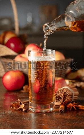Apple cider is poured from a bottle into a glass. Fresh drink with apples, cinnamon, and anise on a kitchen table.