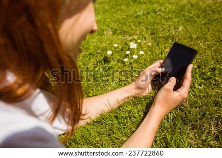 Pretty redhead text messaging on her phone lying on grass
