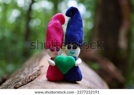 Two toy dwarfs made of plasticine hold a heart. Valentine's Day. A symbol of love.