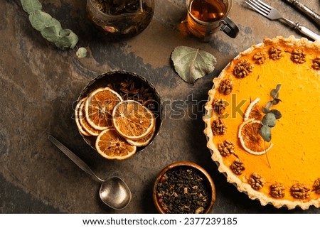 thanksgiving still life, garnished pumpkin pie near dried orange slices and spices on stone surface