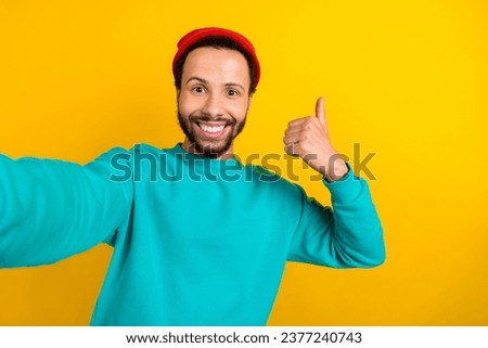 Photo of positive cheerful guy wear teal sweatshirt red beanie hat doing selfie show thumb up good job isolated on yellow color background