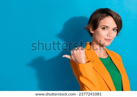 Portrait of young promoter woman wear orange blazer point finger mockup proposition her content product isolated on blue color background