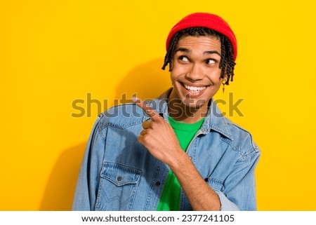 Photo of dreamy charming man wear jeans shirt red hat looking pointing finger empty space isolated yellow color background